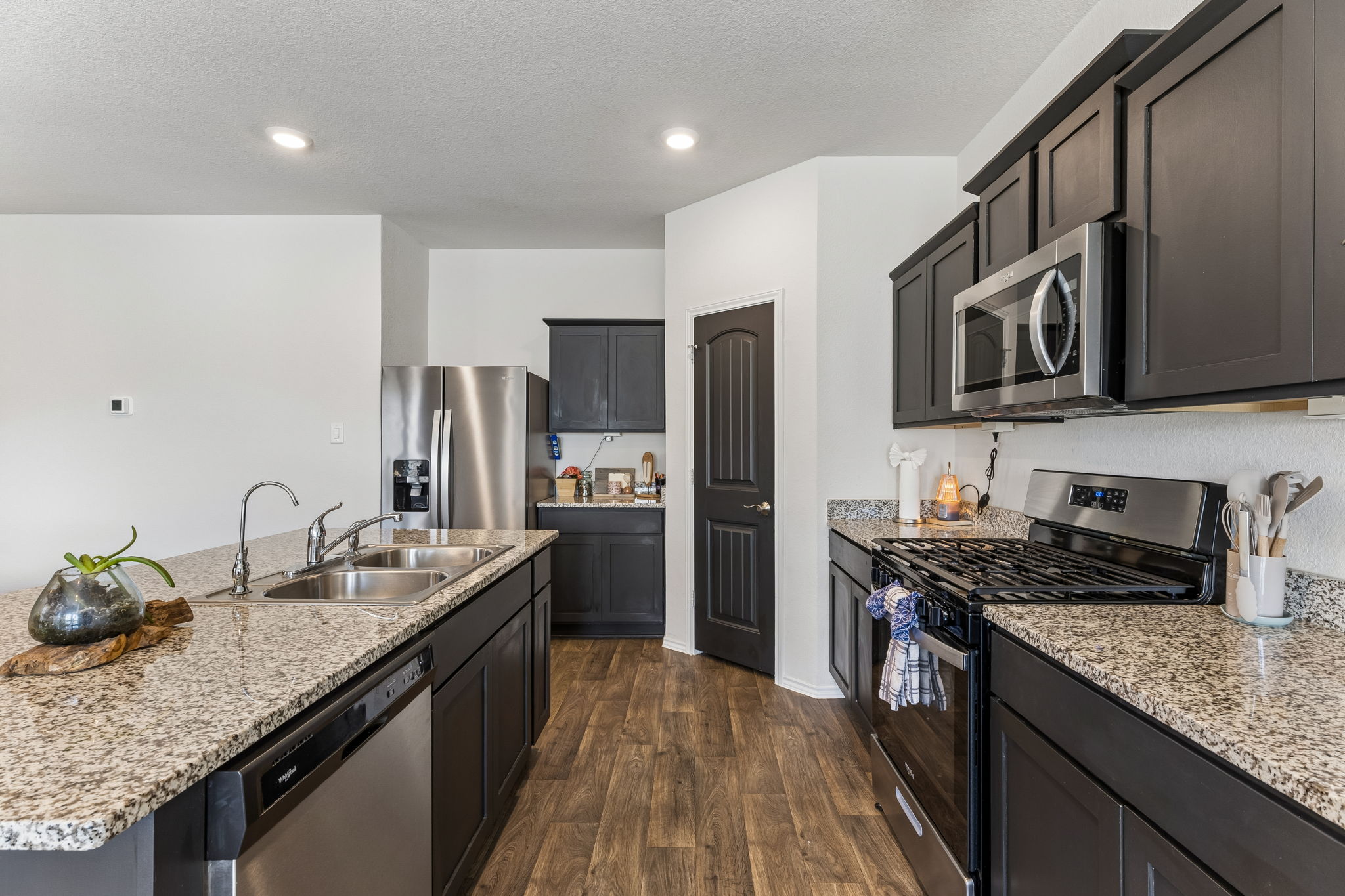 343 Sickle Loop Kyle, TX 78640 - Photo 15 of 40 Modern kitchen featuring dark cabinetry, stainless steel appliances, speckled stone countertops, and wood-finish flooring