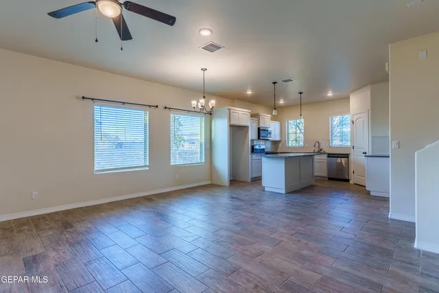 an empty room with wooden floor chandelier and windows