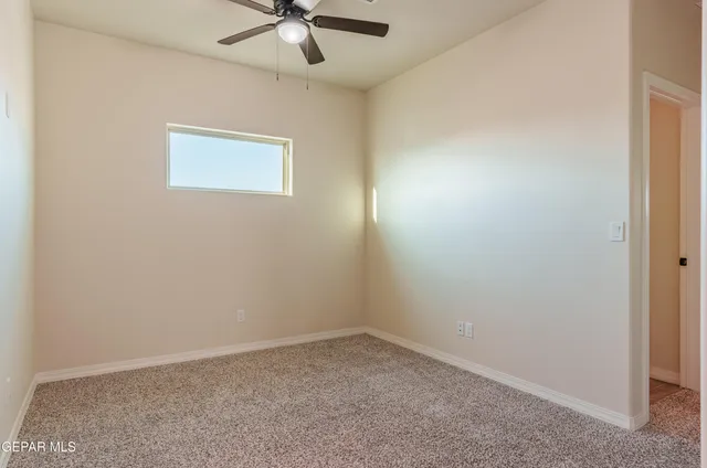 an empty room with chandelier fan and windows
