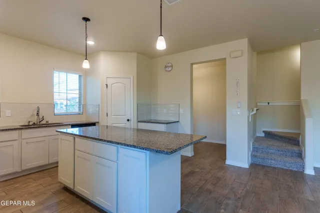 a kitchen with kitchen island granite countertop a refrigerator a sink dishwasher a stove and white cabinets with wooden floor