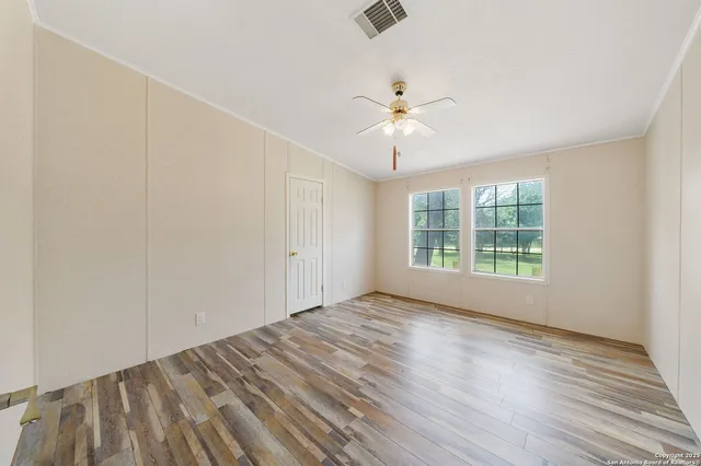 an empty room with wooden floor fan and windows