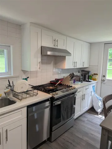 a kitchen with stainless steel appliances granite countertop a stove a sink dishwasher and white cabinets with wooden floor