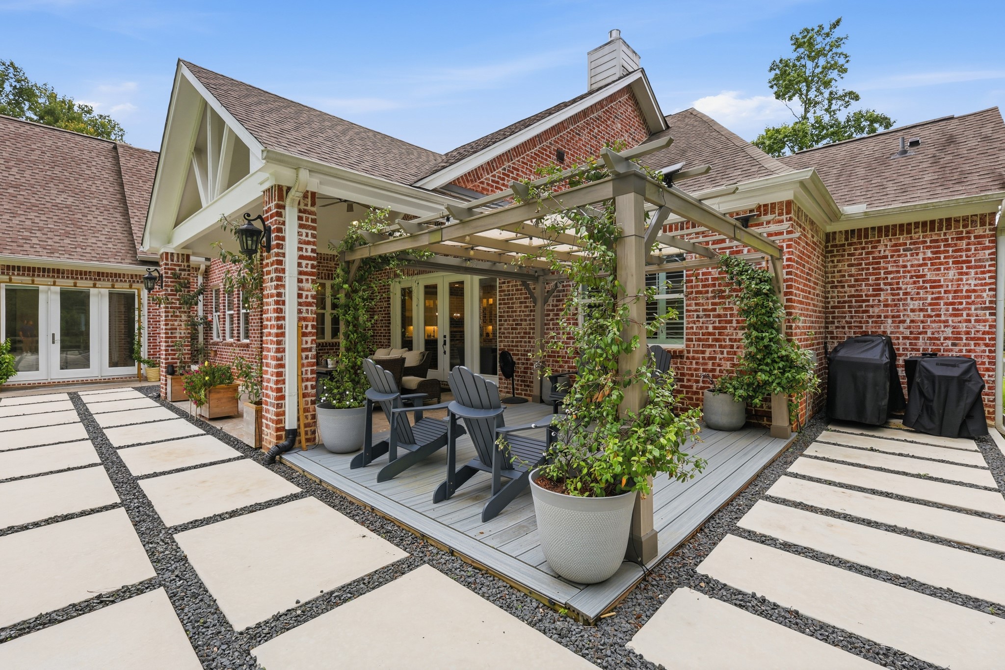 7106 Hampton Court Spring, TX 77389 - Photo 5 of 31 Inviting backyard patio with a pergola-covered seating area, surrounded by lush greenery. The red brick exterior complements the modern, paved walkway, creating a perfect space for relaxation and entertaining.
