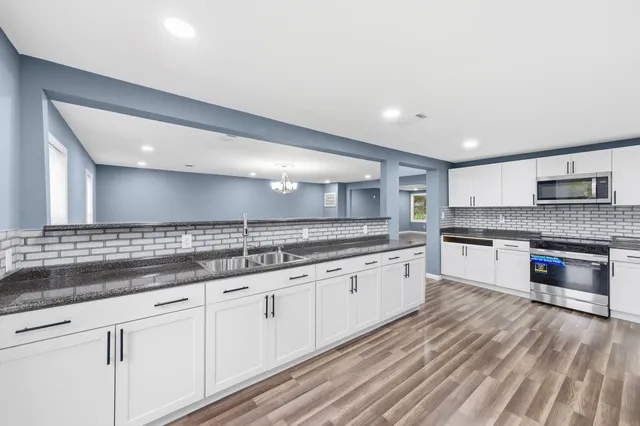 a large white kitchen with granite countertop a stove top oven a sink and dishwasher with wooden floor