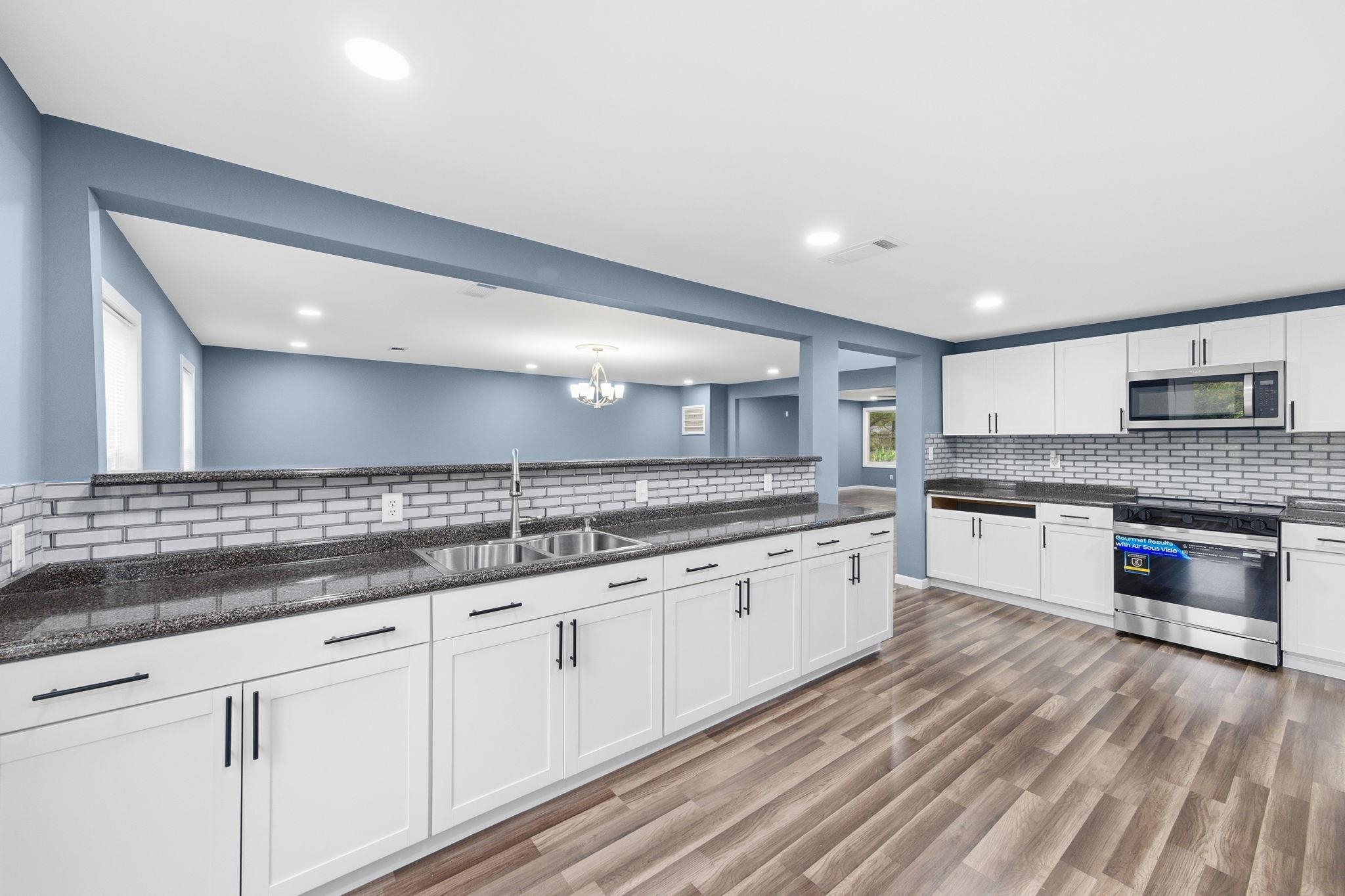 9509 Merrill Road Millington, TN 38053 - Photo 14 of 26 a large white kitchen with granite countertop a stove top oven a sink and dishwasher with wooden floor