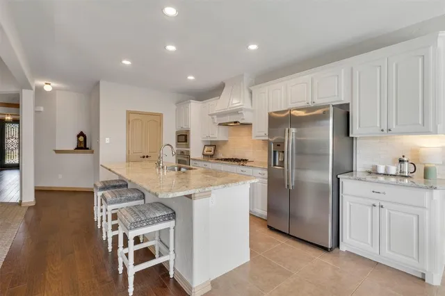 a kitchen with stainless steel appliances granite countertop a refrigerator a sink a stove and white cabinets with wooden floor