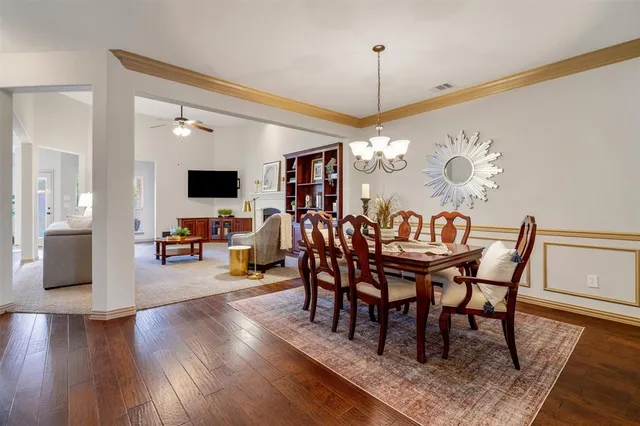 a view of a dining room and livingroom with furniture wooden floor a rug a flat screen tv a painting and a chandelier