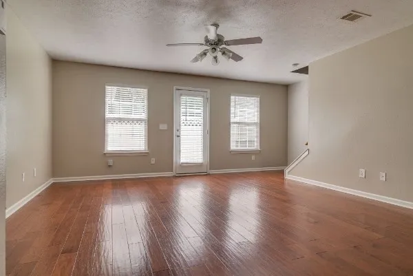 an empty room with wooden floor chandelier fan and windows