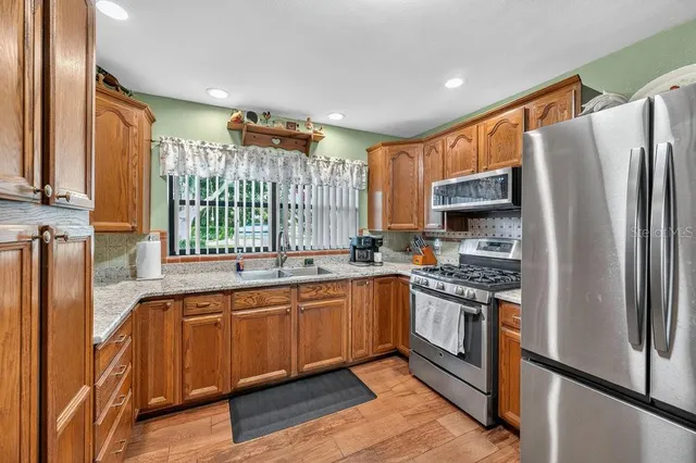 a kitchen with stainless steel appliances granite countertop a refrigerator a sink dishwasher a stove and white countertops with wooden floor