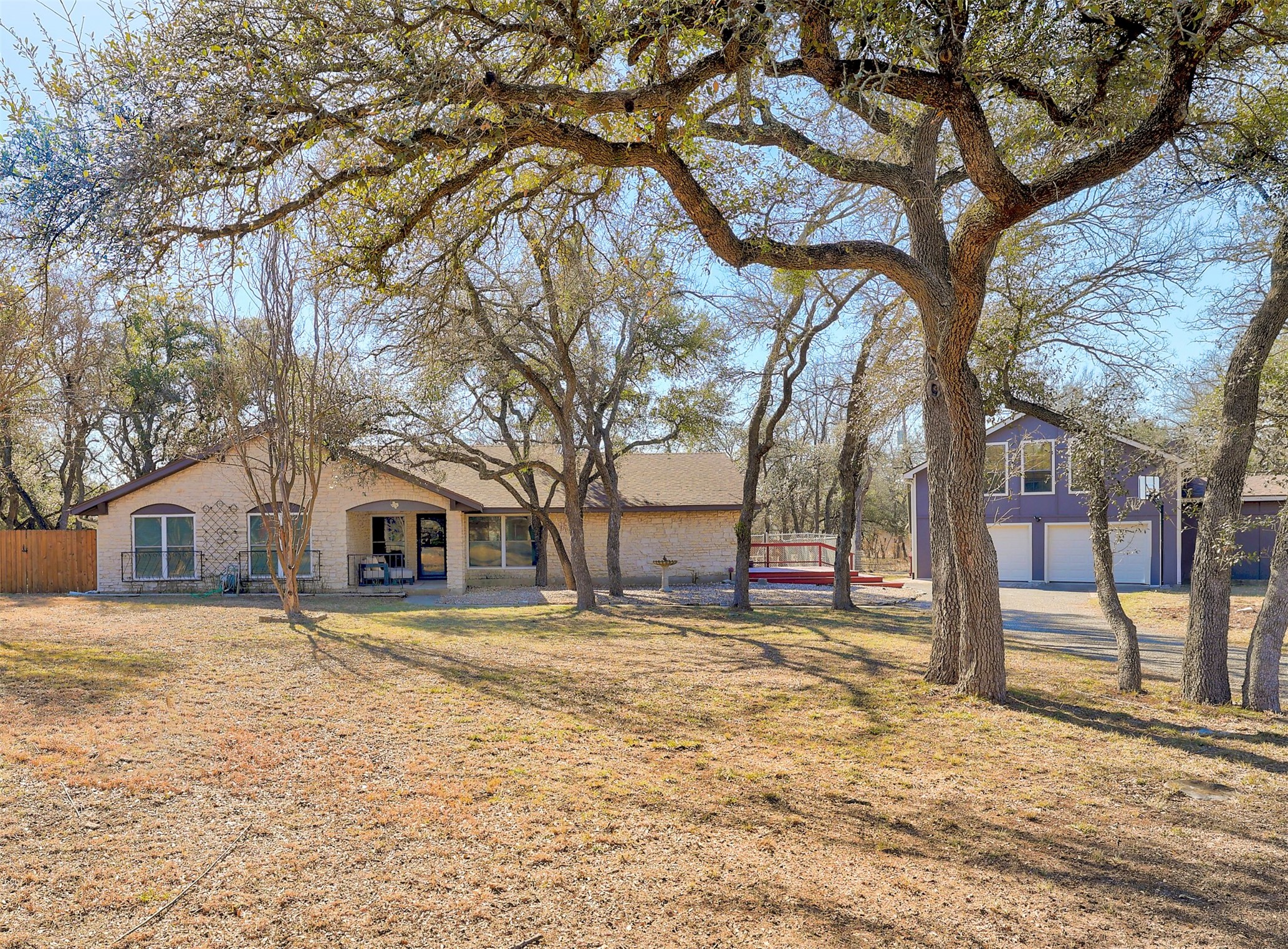 Tree filled lot with front view of home and 4- car garage building to the left