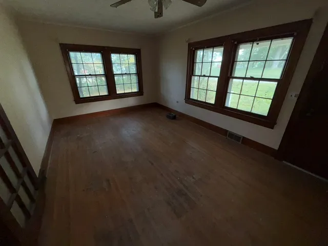 a view of an empty room with wooden floor and fan
