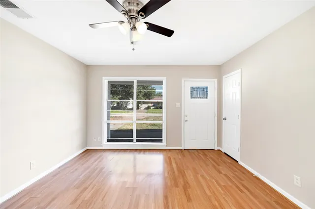 an empty room with wooden floor chandelier fan and windows