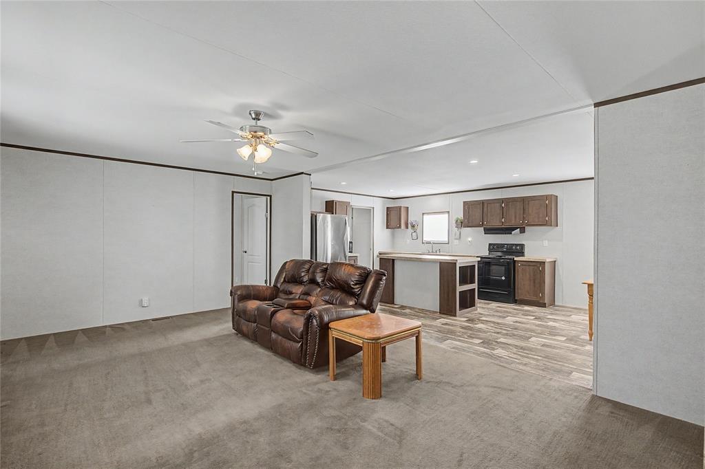 177 New Highland Road Springtown, TX 76082 - Photo 8 of 40 Open-concept living space featuring a ceiling fan with light fixture, light gray carpet, and white wall panels with dark trim