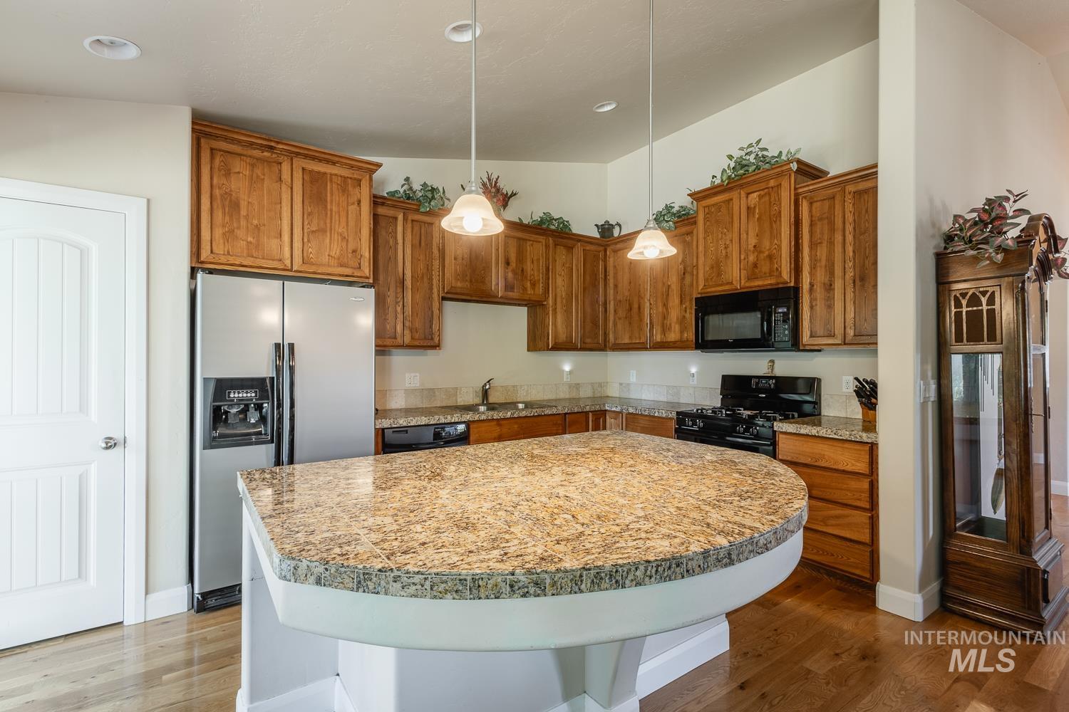 1186 East Observation Street Meridian, ID 83642 - Photo 14 of 33 Kitchen featuring a granite-topped island, wood-finish cabinetry, stainless steel refrigerator, black gas range, and wood-finish flooring