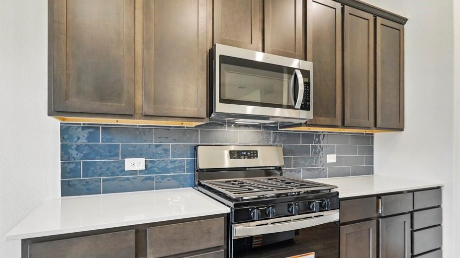 4162 Waldron Trail Forney, TX 75126 - Photo 5 of 29 Kitchen featuring stainless steel appliances, dark wood-finish cabinetry, light-toned countertops, and a blue subway tile backsplash