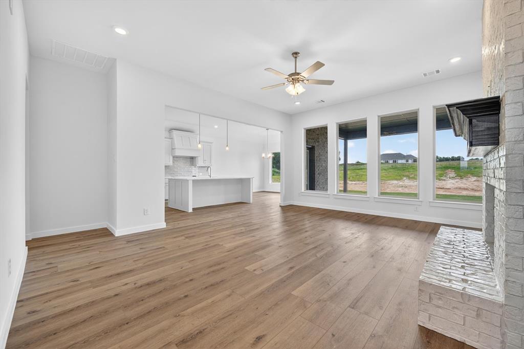 416 McAlpine Drive Springtown, TX 76082 - Photo 7 of 40 Open-concept living area featuring wood-finish flooring, a stone-clad fireplace, and a ceiling fan with integrated lighting