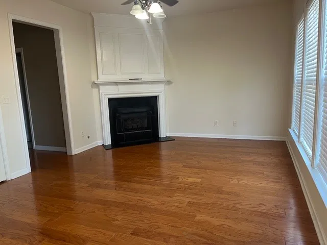 an empty room with wooden floor fireplace and windows
