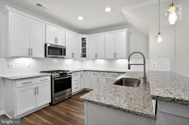 a kitchen with stainless steel appliances granite countertop a refrigerator a sink a stove and white cabinets with wooden floor