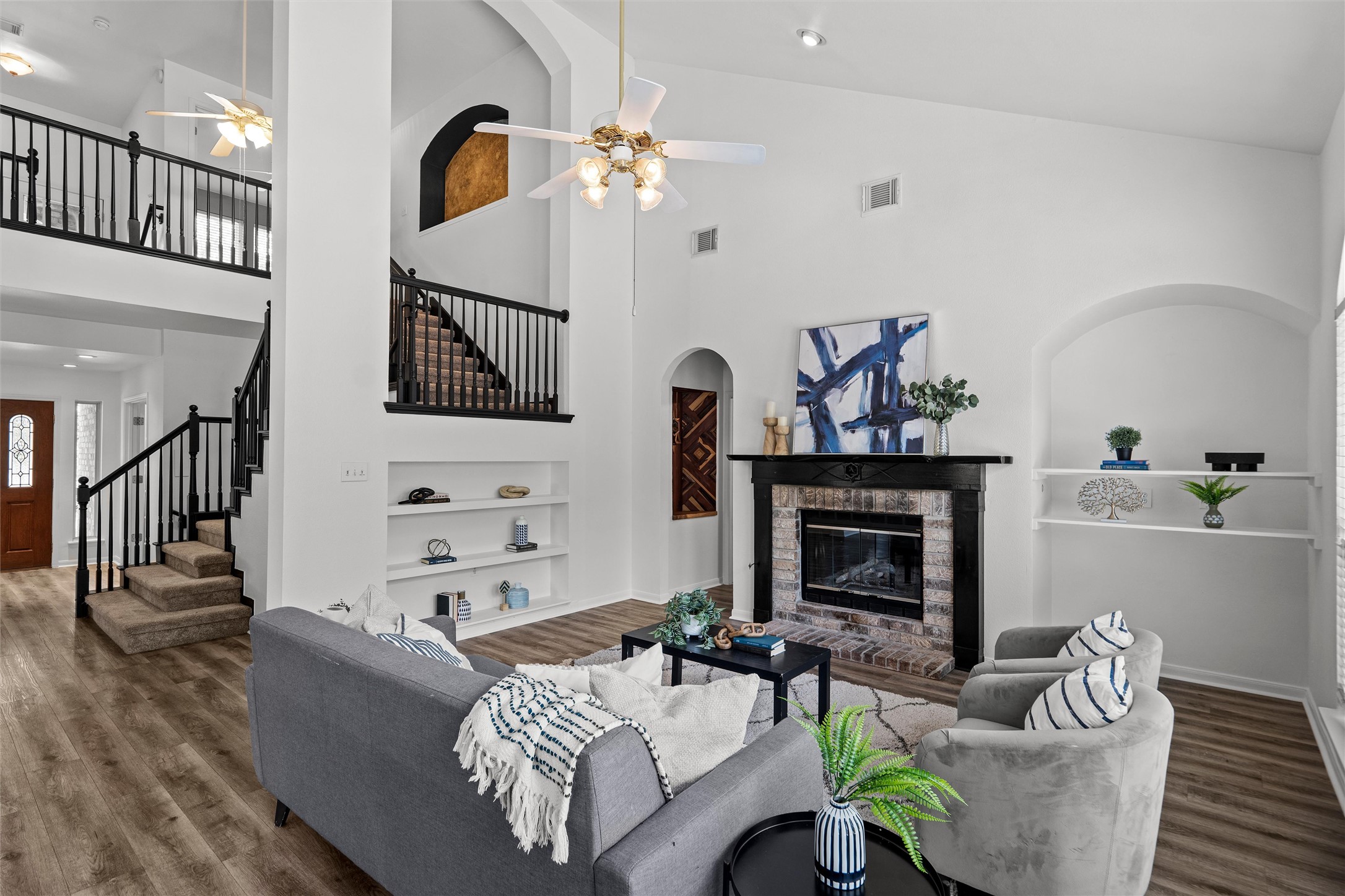 A soaring living area showcases rich wood flooring, a stately brick fireplace, and built-in shelving.