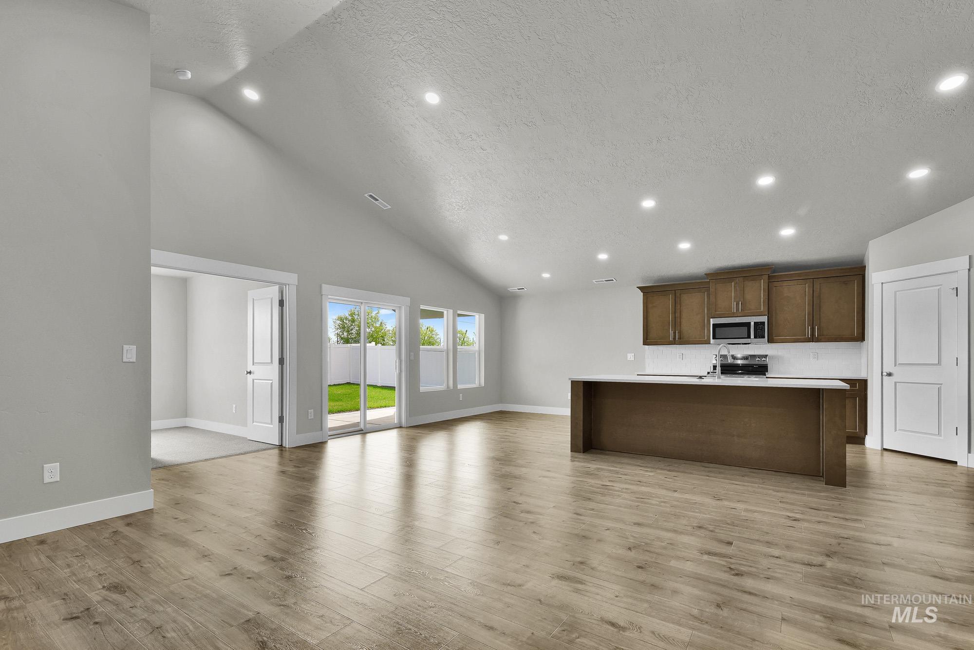 320 North 12th Parma, ID 83660 - Photo 19 of 34 Spacious living area featuring vaulted ceilings, recessed lighting, wood-finish flooring, a kitchen island with light-toned countertops, and sliding glass doors opening to a fenced backyard