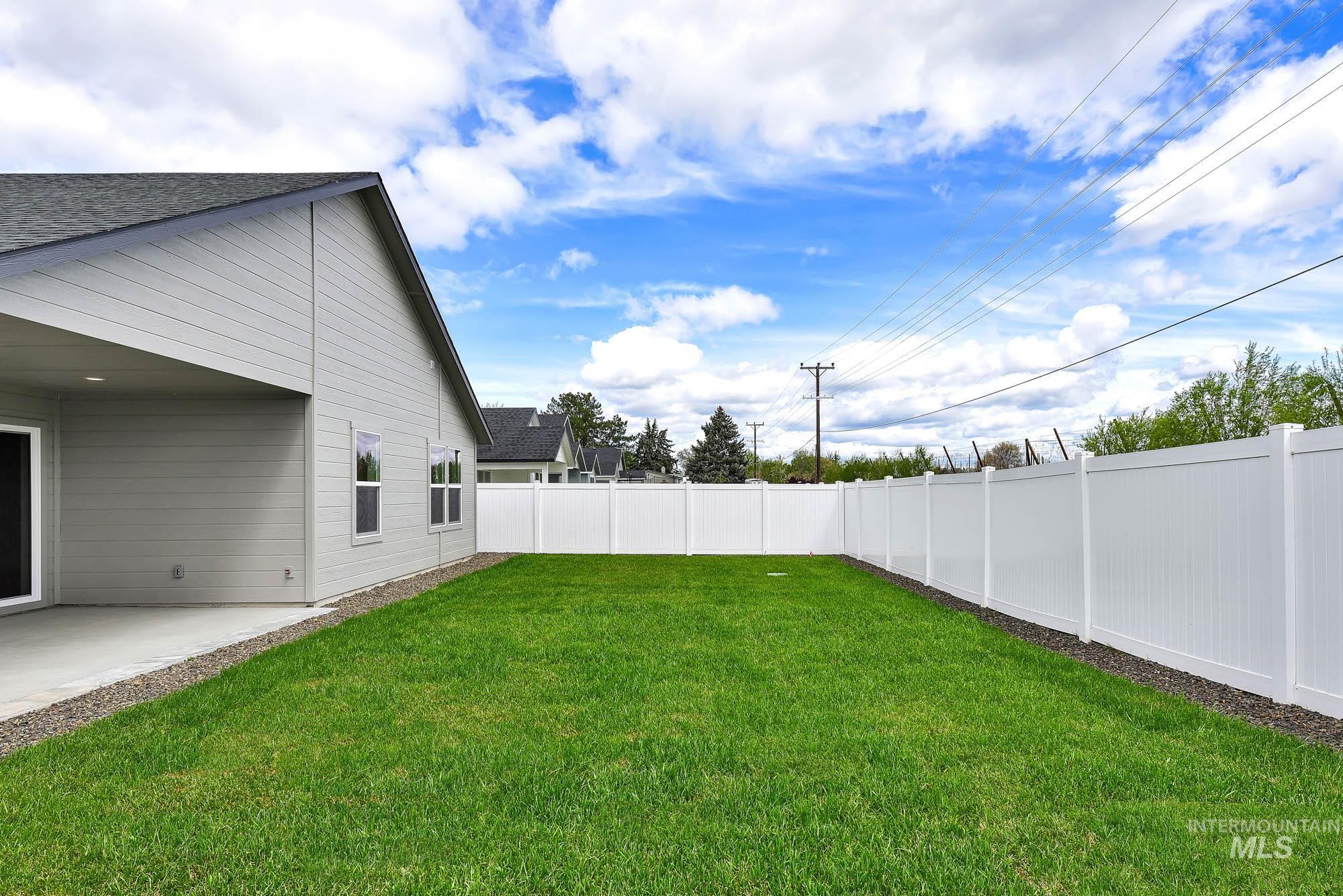 320 North 12th Parma, ID 83660 - Photo 34 of 34 Expansive backyard featuring a lush green lawn, full white privacy fencing, and a covered concrete patio