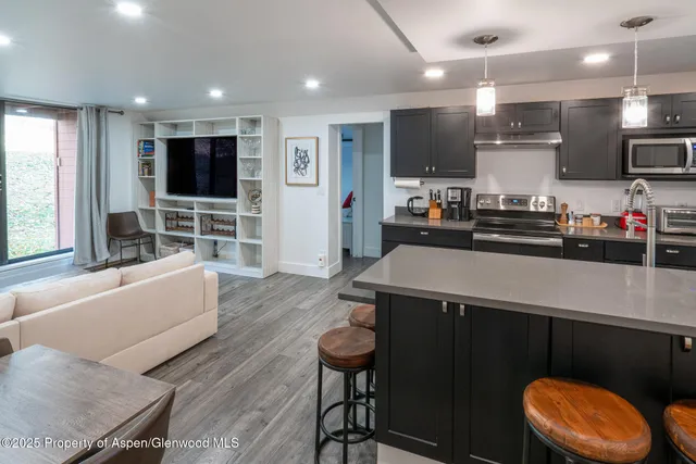 a kitchen with stainless steel appliances kitchen island granite countertop a refrigerator a stove a microwave oven a dining table and chairs with wooden floor