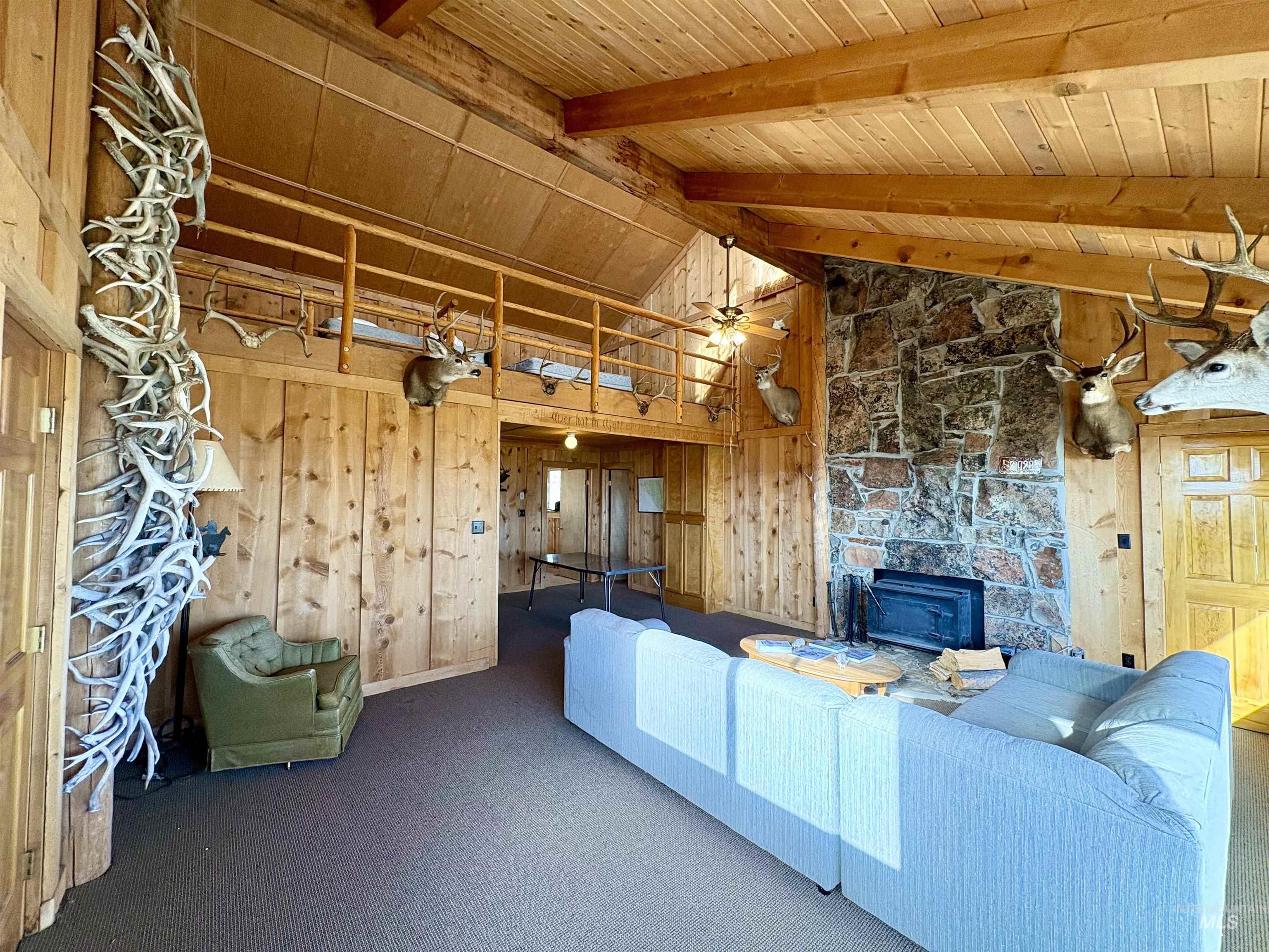 2040 Pahsimeroi River Road May, ID 83253 - Photo 11 of 29 Spacious living area featuring a vaulted wood-paneled ceiling with exposed beams, a stone-clad fireplace, and wood-paneled walls