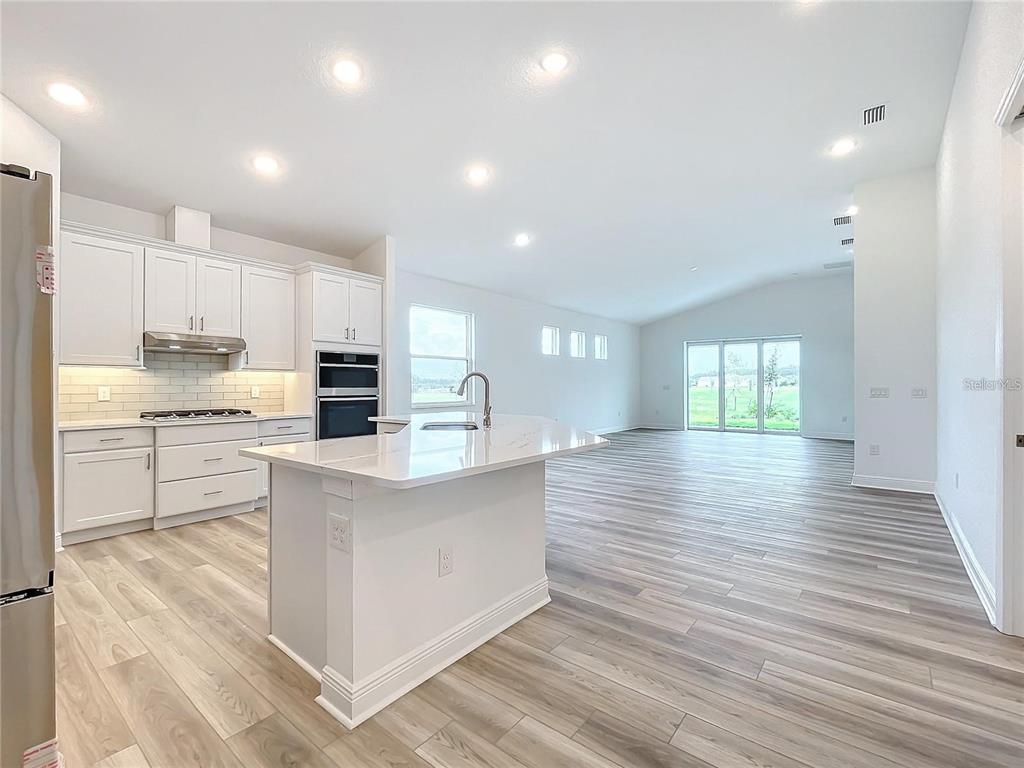3951 Kennebunk Loop Mount Dora, FL 32757 - Photo 10 of 54 a large kitchen with kitchen island a sink dishwasher a stove and a refrigerator with wooden floor