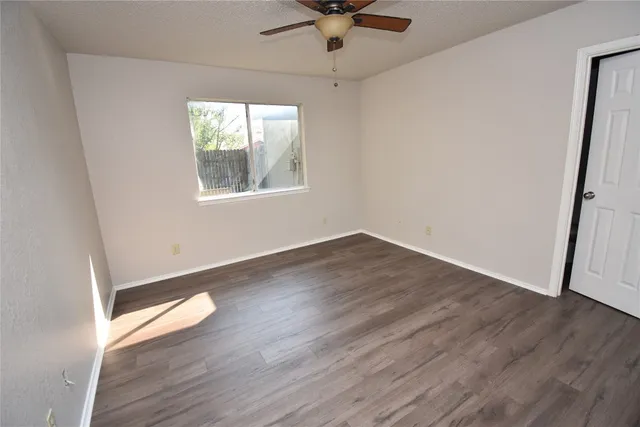 an empty room with wooden floor fan and windows