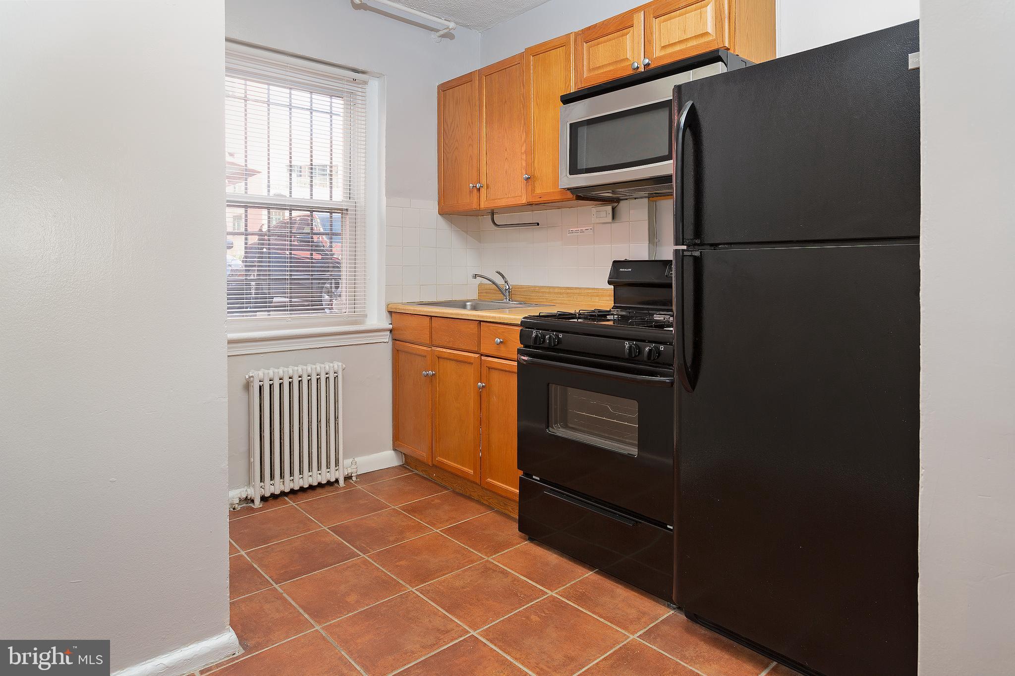 2415 Ontario Road Northwest, Unit 101 Washington, DC 20009 - Photo 6 of 22 a kitchen with granite countertop a refrigerator stove and microwave