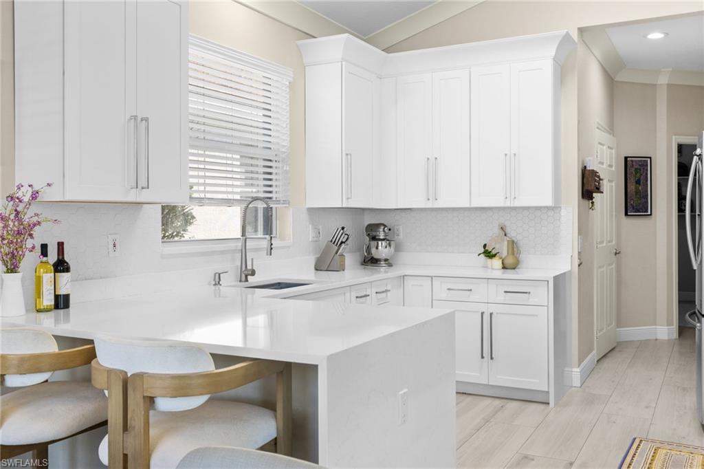 1869 Pondside Lane Naples, FL 34109 - Photo 9 of 34 Kitchen with a peninsula, white cabinetry, a breakfast bar area, decorative backsplash, and lofted ceiling