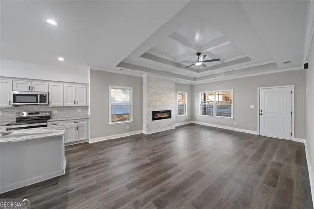an empty room with wooden floor a ceiling fan a kitchen view and a window