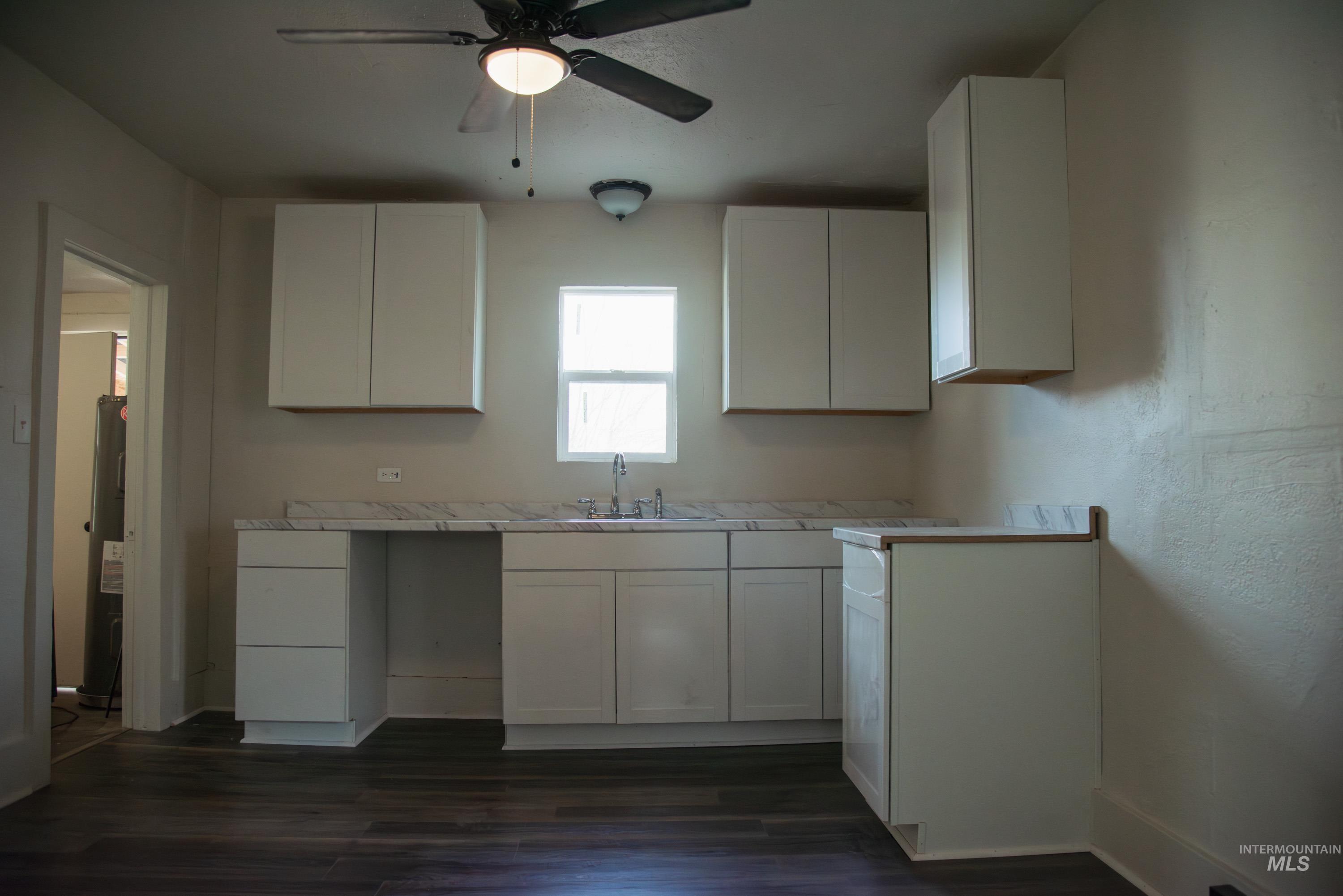 907 North 7th Street Payette, ID 83661 - Photo 11 of 15 Kitchen featuring light countertops, white cabinetry, dark wood-style floors, electric water heater, and ceiling fan