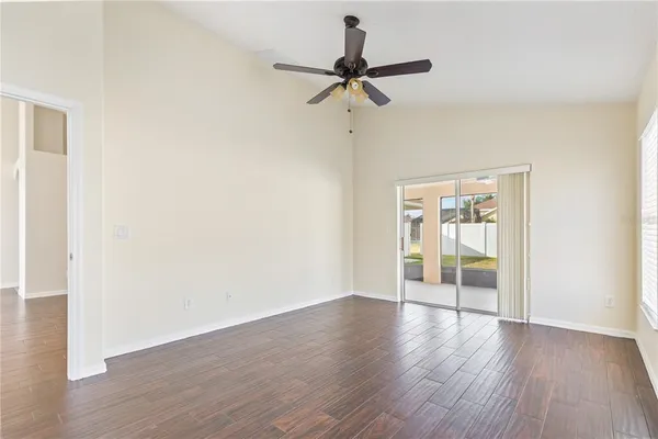 an empty room with wooden floor chandelier fan and windows