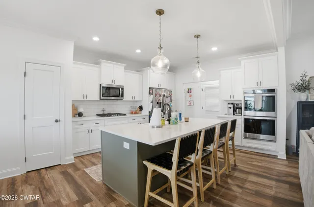 a kitchen with stainless steel appliances kitchen island granite countertop a dining table chairs sink and white cabinets