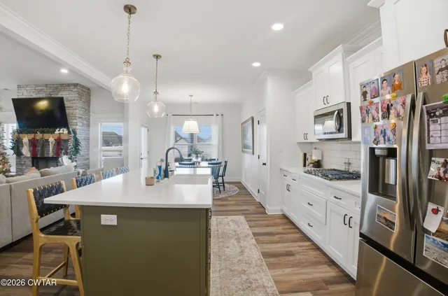 a large kitchen with stainless steel appliances kitchen island granite countertop a refrigerator a sink dishwasher a dining table and chairs with wooden floor