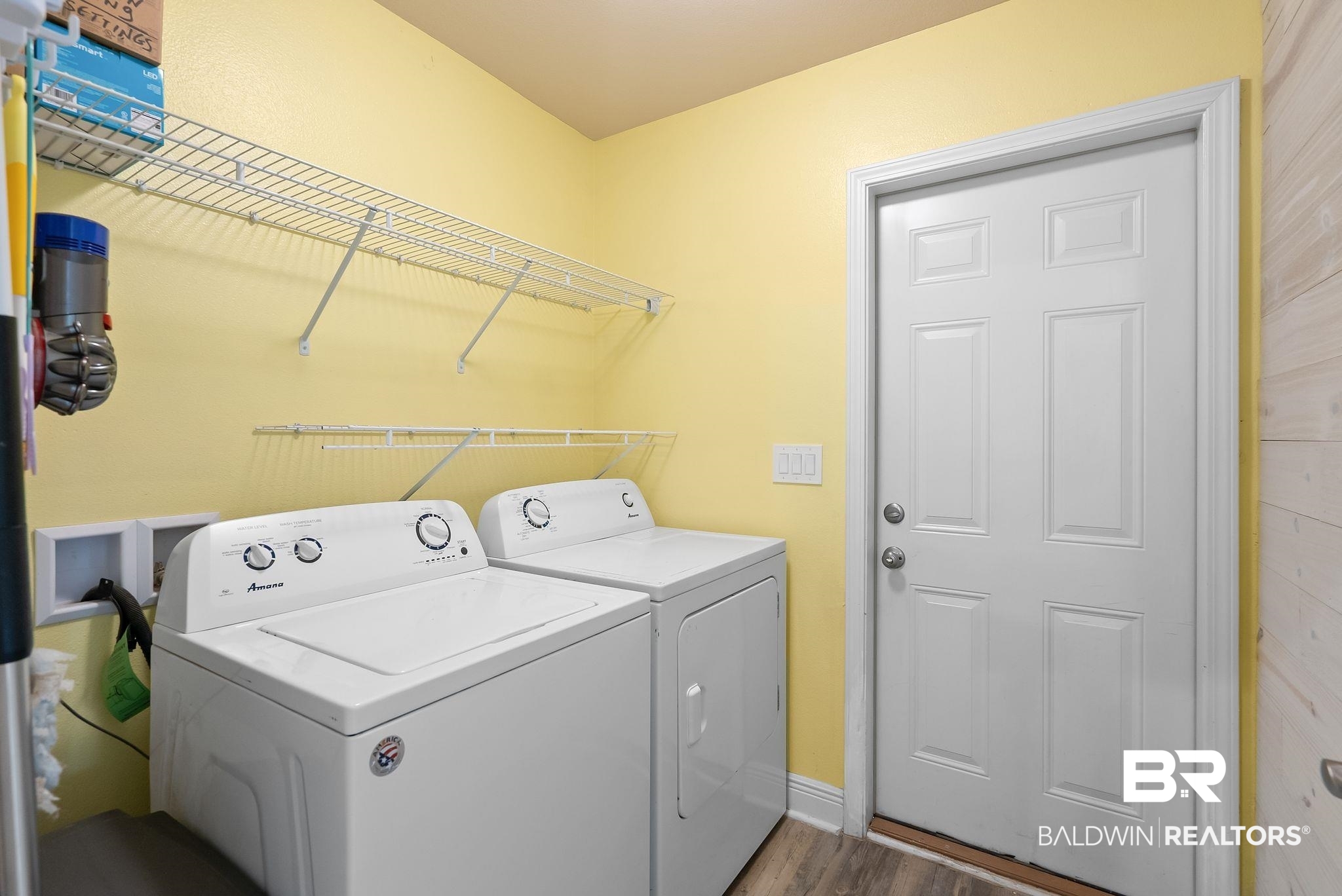 22076 Garland Loop Silverhill, AL 36576 - Photo 18 of 27 Dedicated laundry area featuring wire shelving, wood-finish flooring, a paneled door, and light yellow walls
