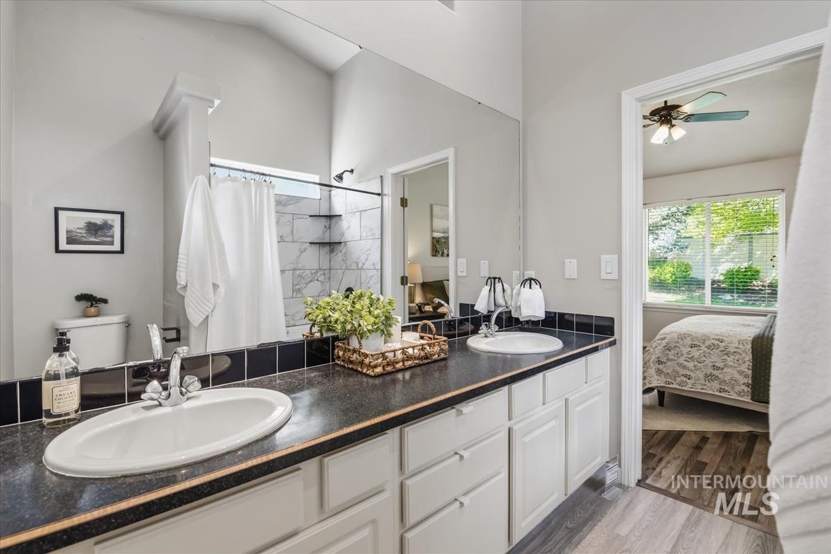 802 North Echohawk Way Eagle, ID 83616 - Photo 12 of 30 Vaulted ceiling bathroom featuring a double vanity with dark countertops, white cabinetry, a large mirror, and a shower with white tile surround