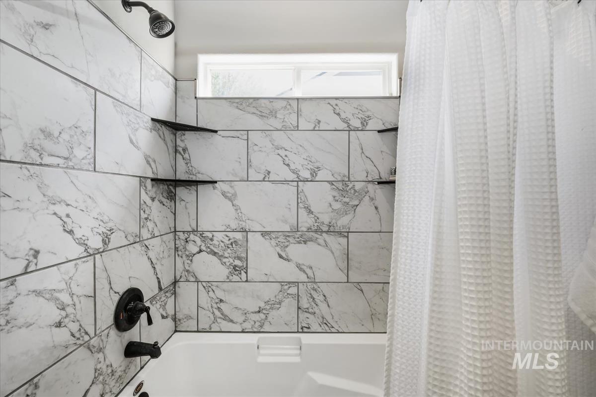 802 North Echohawk Way Eagle, ID 83616 - Photo 10 of 30 Bathtub with marble-patterned tile surround, matte black fixtures, built-in corner shelving, and an upper transom window