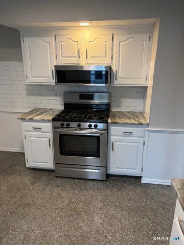 a kitchen with granite countertop a stove a microwave a sink and cabinets