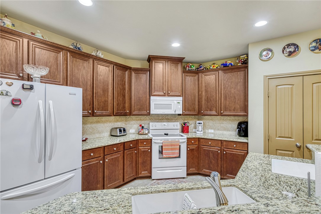9945 Oxford Cemetery Road Madisonville, TX 77864 - Photo 12 of 42 Kitchen featuring white appliances, decorative backsplash, light stone countertops, recessed lighting, and brown cabinets