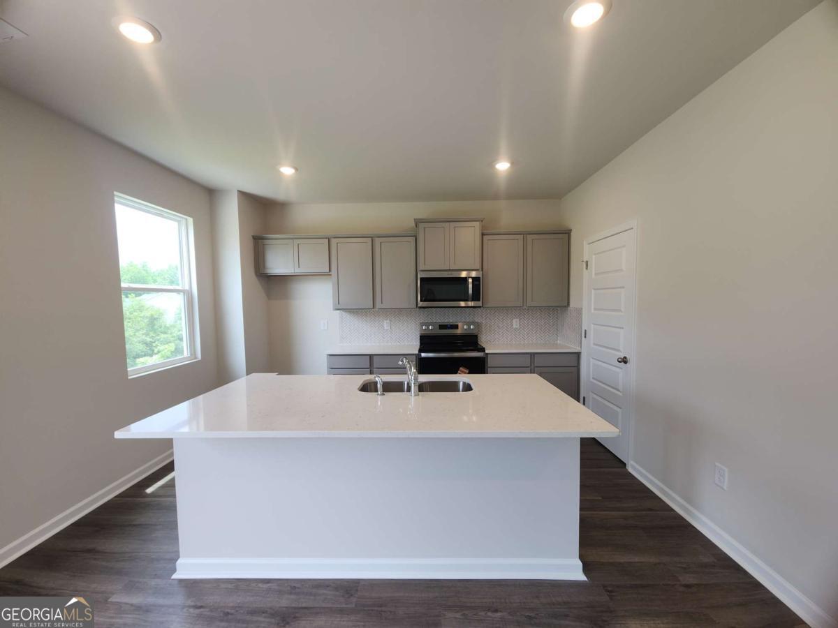 146 Aster Avenue Locust Grove, GA 30248 - Photo 8 of 25 a large kitchen with kitchen island a sink wooden floor and white appliances