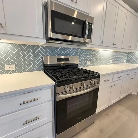 a kitchen with stainless steel appliances granite countertop white cabinets and a stove top oven