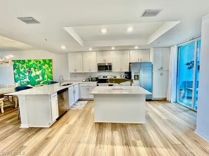 a large kitchen with stainless steel appliances a large counter top a stove a refrigerator cabinets and living room view