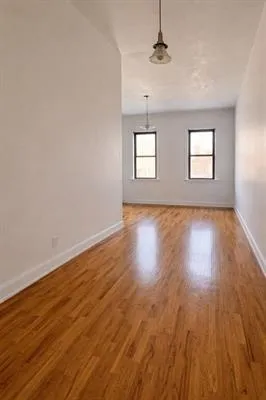 an empty room with wooden floor chandelier and windows