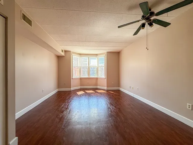 an empty room with wooden floor fan and windows