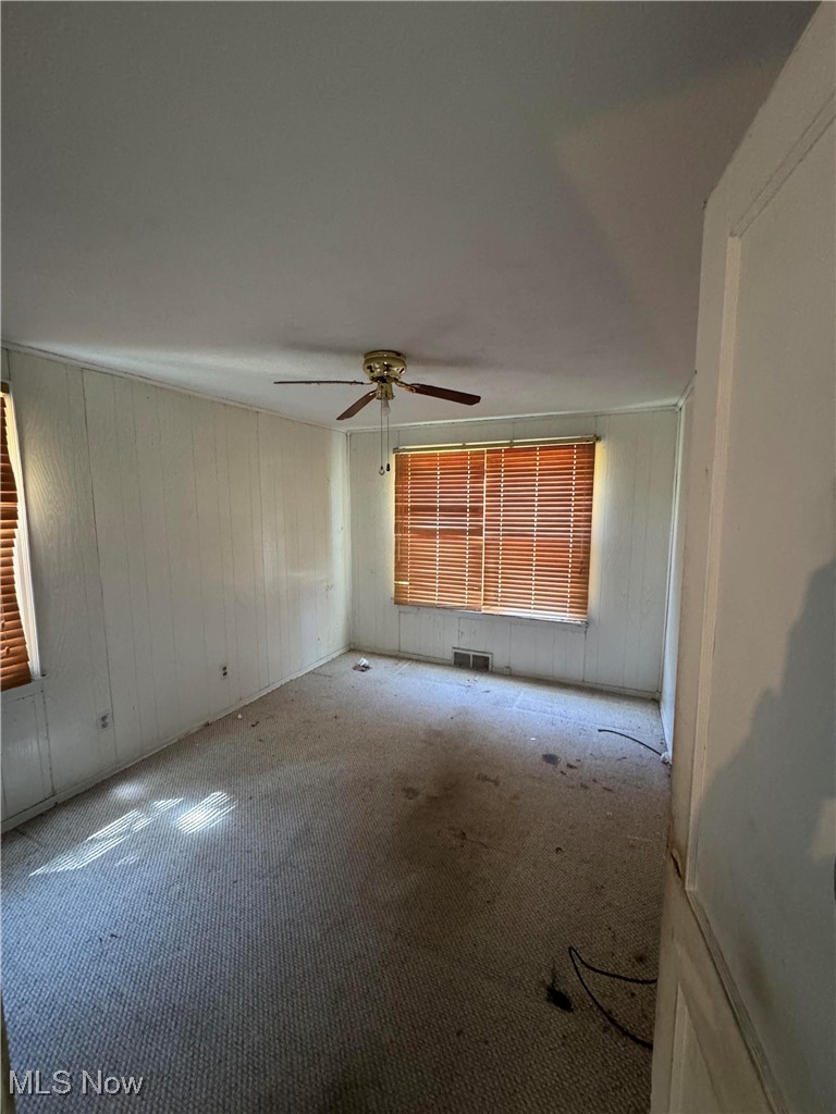 8133 Midland Road Mentor, OH 44060 - Photo 2 of 4 Empty room with a ceiling fan, carpet flooring, wood walls, and visible vents