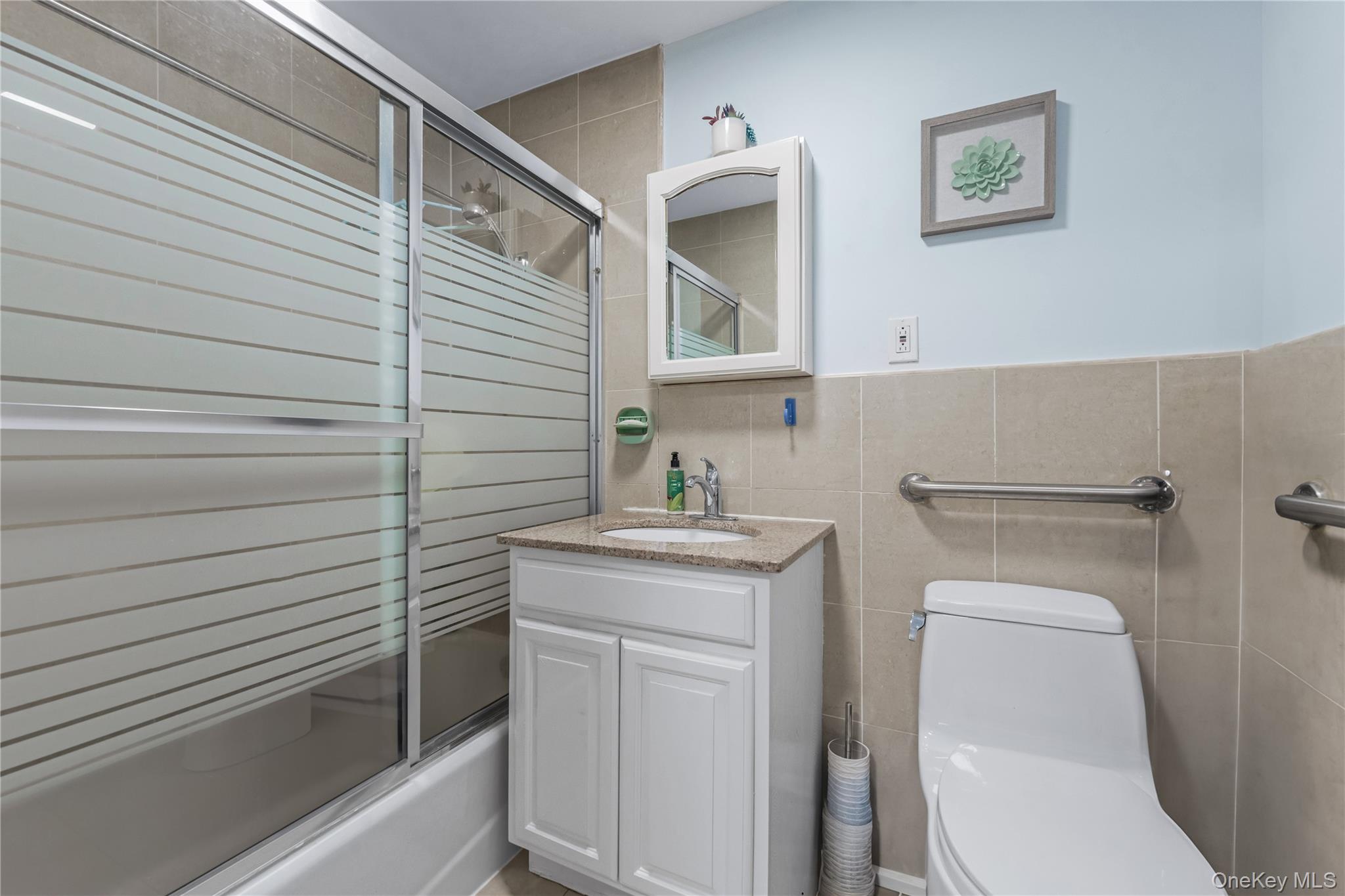 35-06 Leavitt Street, Unit 3K Queens, NY 11354 - Photo 11 of 17 Bathroom with shower / bath combination with glass door, vanity, tile walls, and wainscoting