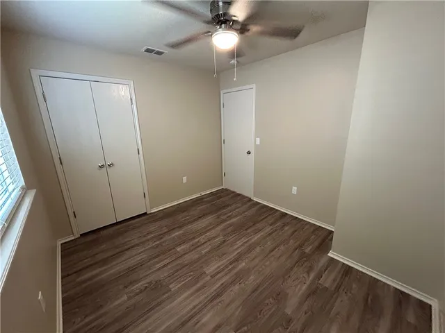 a view of an empty room with wooden floor and a ceiling fan