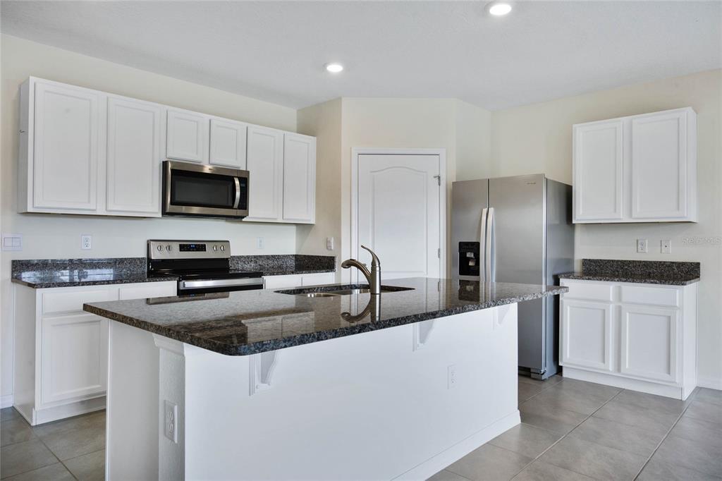 652 Greymount Street Davenport, FL 33837 - Photo 7 of 30 a kitchen with stainless steel appliances granite countertop a sink a stove a refrigerator a microwave and cabinets
